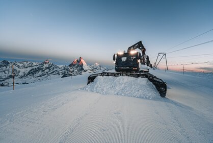 Pistenfahrzeug verteilt Schnee in der Morgendämmerung. Die ersten Sonnenstrahlen lassen das Matterhorn rot erscheinen | © Zermatt Bergbahnen