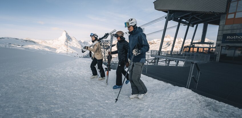 Drei Skifahrer laufen von der Rothorn Bahn zur Piste.  | © Zermatt Bergbahnen