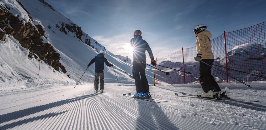 Three skiers skiing towards the sun.  | © Zermatt Bergbahnen