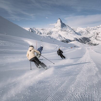 Drei Skifahrer fahren auf frisch präparierten Piste im Matterhorn Ski Paradise. Im Vordergrund ist das Matterhorn ersichtlich. | © Zermatt Bergbahnen