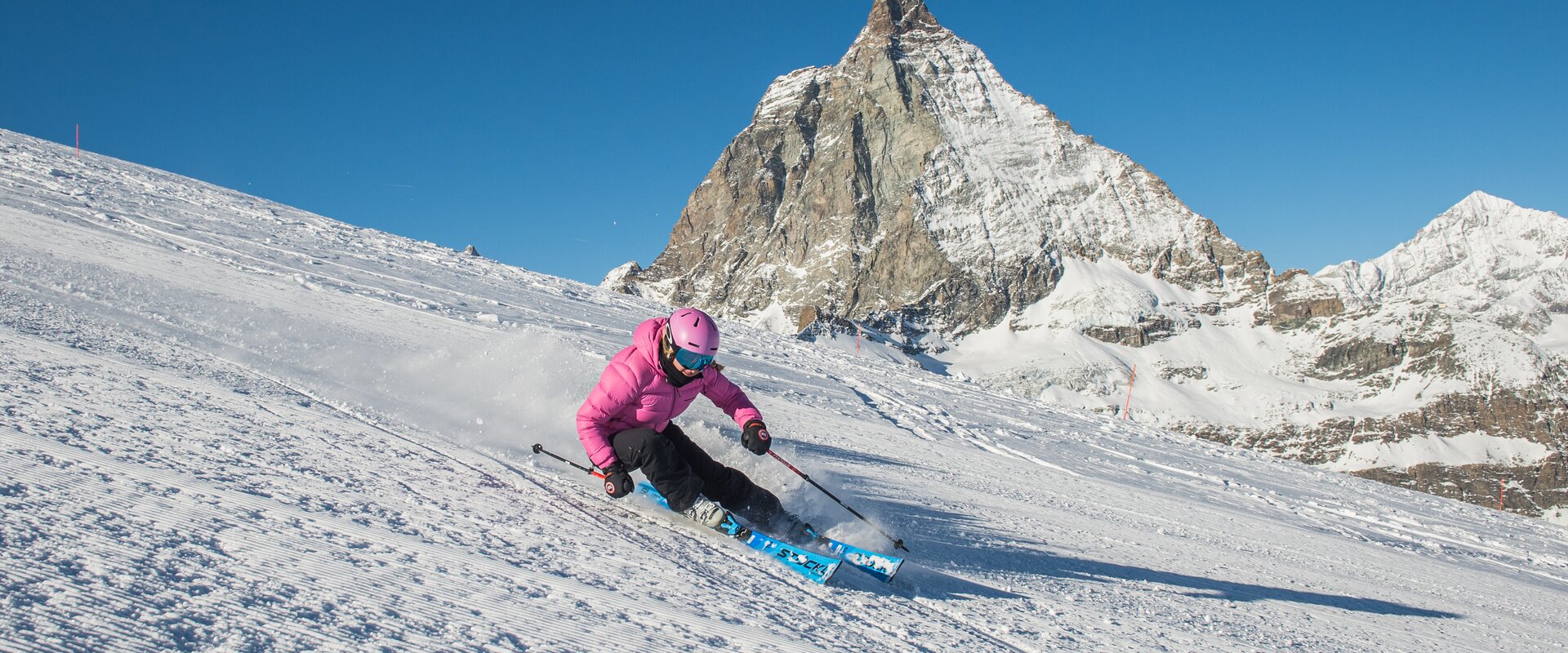 Frau mit pinker Jacke fährt den Furggsattel hinunter, im Hintergrund das Matterhorn | © Michi Portmann