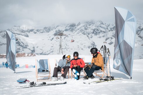 Drei Personen unterhalten sich im Snowpark auf den Liegestühlen.  | © Basic Home Production