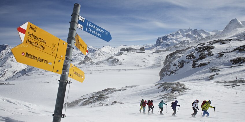 Groupe de raquetteurs se frayant un chemin dans la neige, avec un panneau indicateur au premier plan. | © Michi_Portmann