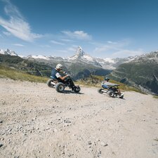 Two men hurtle down the path on mountain carts with the Matterhorn in the background. | © Gabriel Perren