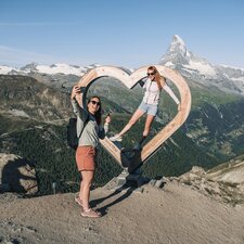 Two women take a selfie in front of the wooden heart on Blauherd.  | © Gabriel Perren